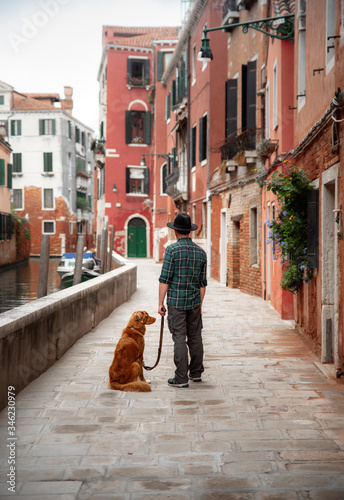 A man with a dog on a waterfront in Venice. Traveling with a pet. Nova Scotia Duck Tolling Retriever with the city