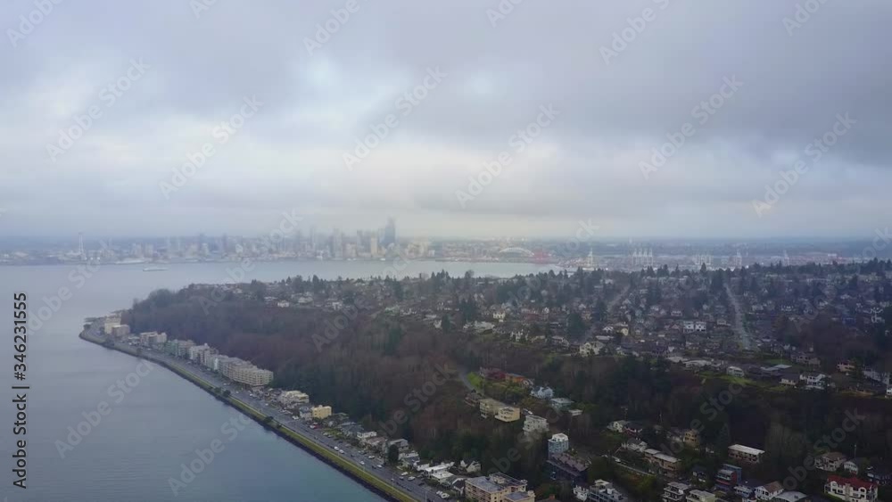 Beautiful Scenery Of Lush Trees In Alki Beach Surrounded By The Calm Sea In Washington With The City Of Seattle In The Background - Aerial Shot Beautiful Scenery Of Lush Trees In Alki Beach Surrounded By The Calm Sea In Washington With The City Of Seattle In The Background - Aerial Shot