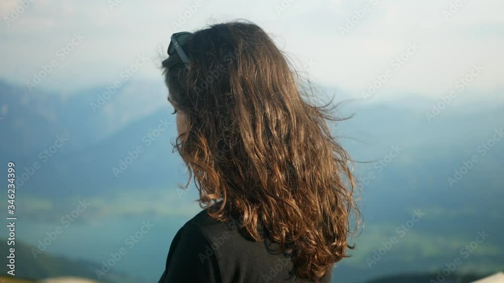 Pretty hiker girl looking at epic view at Schafberg mountain in Salzkammergut Austria. 60fps slowmo footage at alpine dramatic peak wind blowing her hair. Lake in background. Brunette sexy woman Pretty hiker girl looking at epic view at Schafberg mountain in Salzkammergut Austria. 60fps slowmo footage at alpine dramatic peak wind blowing her hair. Lake in background. Brunette sexy woman