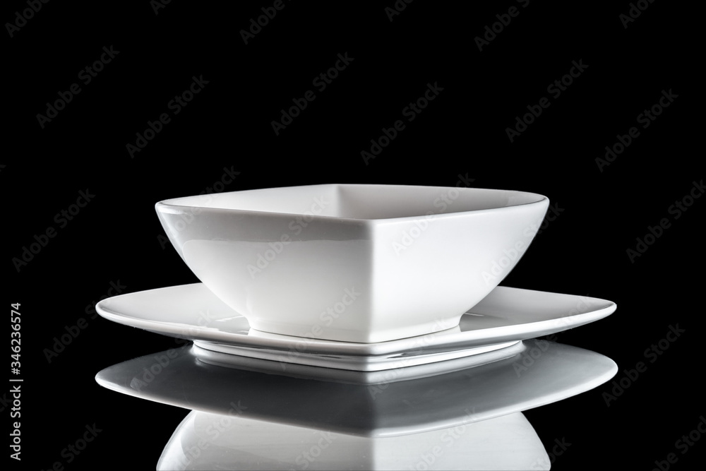 Dishes isolated on black. Square white empty plate for dinner on dark background. Clean circle porcelain crockery. Breakfast tableware. Dishes isolated on black. Square white empty plate for dinner on dark background. Clean circle porcelain crockery. Breakfast tableware.
