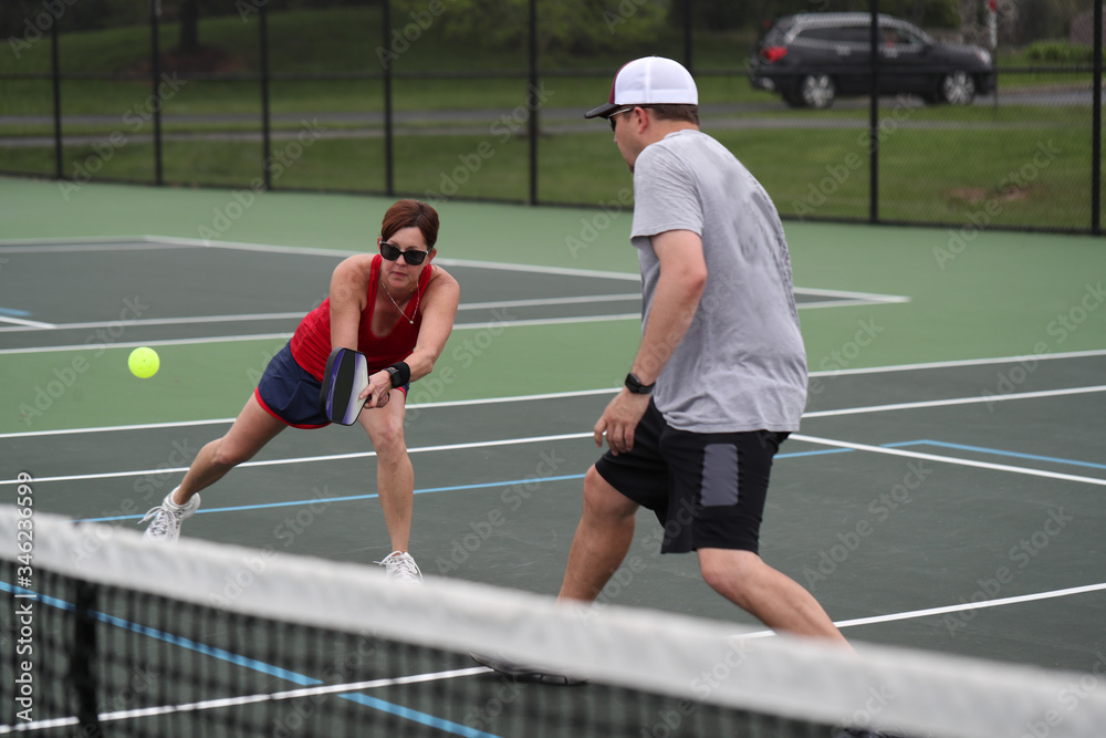 Obraz premium An attractive senior, playing pickleball, hits a two-handed backhand during a mixed doubles match.
