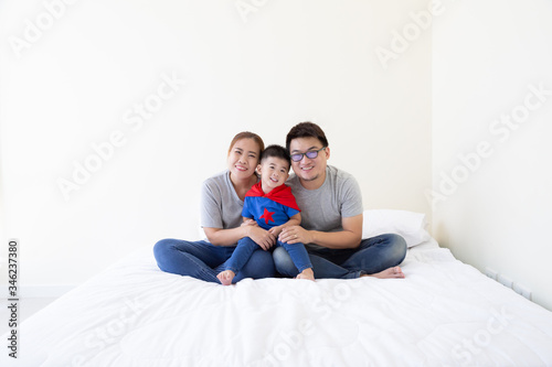 Smiling Happy Asian family and son wearing superhero suit sitting on white bed in the bedroom