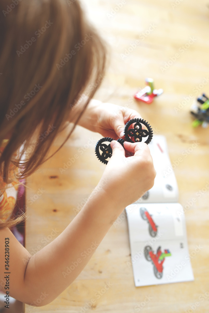 blonde haired young girl assembles gears with her little fingers to ...