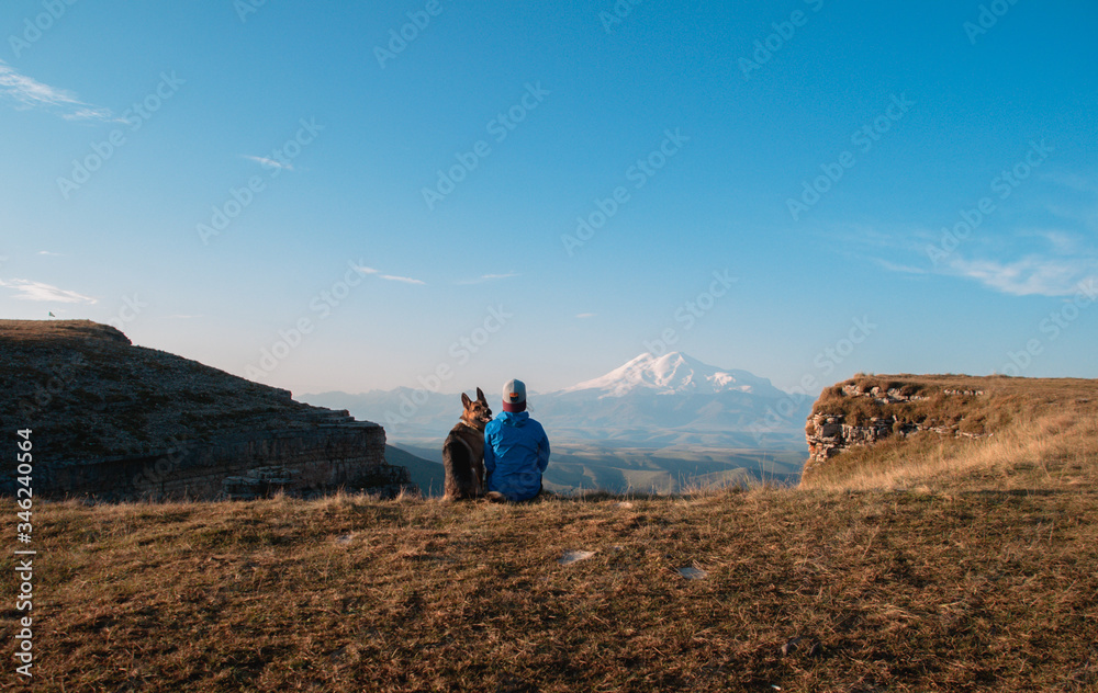 Naklejka premium Girl and dog on the background of Elbrus. A girl and a German shepherd travel through the mountains together.