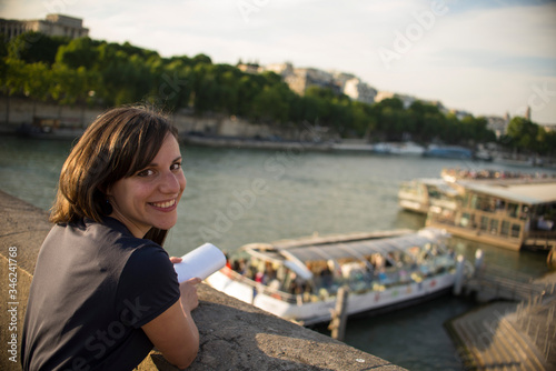 Young smiling tourist looks smiling into camera on the banks of the Seine in Paris.