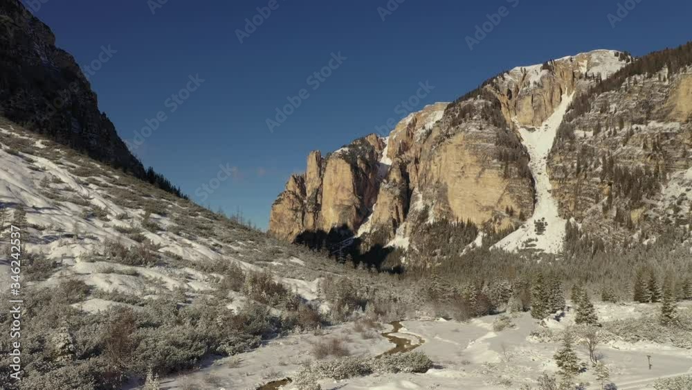 Aerial view of the valley near the Pederu mountain refuge. Narrow snow-covered pass winding through the dense pine forest. Mountains tower around, casting long shadows on the landscape. Aerial view of the valley near the Pederu mountain refuge. Narrow snow-covered pass winding through the dense pine forest. Mountains tower around, casting long shadows on the landscape.