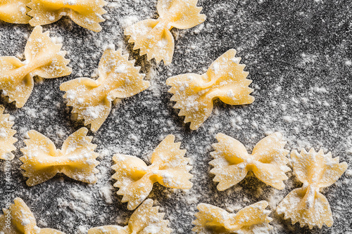 Farfalle sprinkled with flour, hand made on a worn metal table, close-up, top view. Background for the Italian menu. Pasta factory.