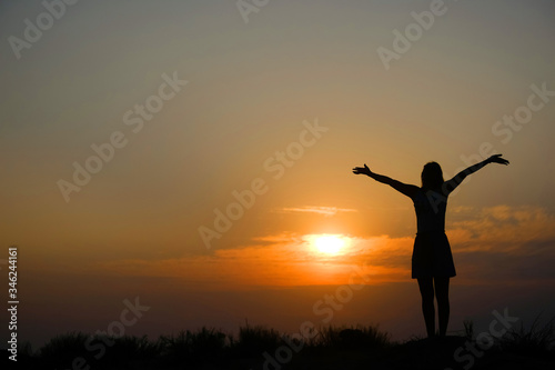 Silhouette of a girl on top of a mountain at sunset.