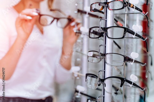 Female is standing with glasses in hands in the background Optical shop. Stand with spectacles. Eyesight correction. Close up.