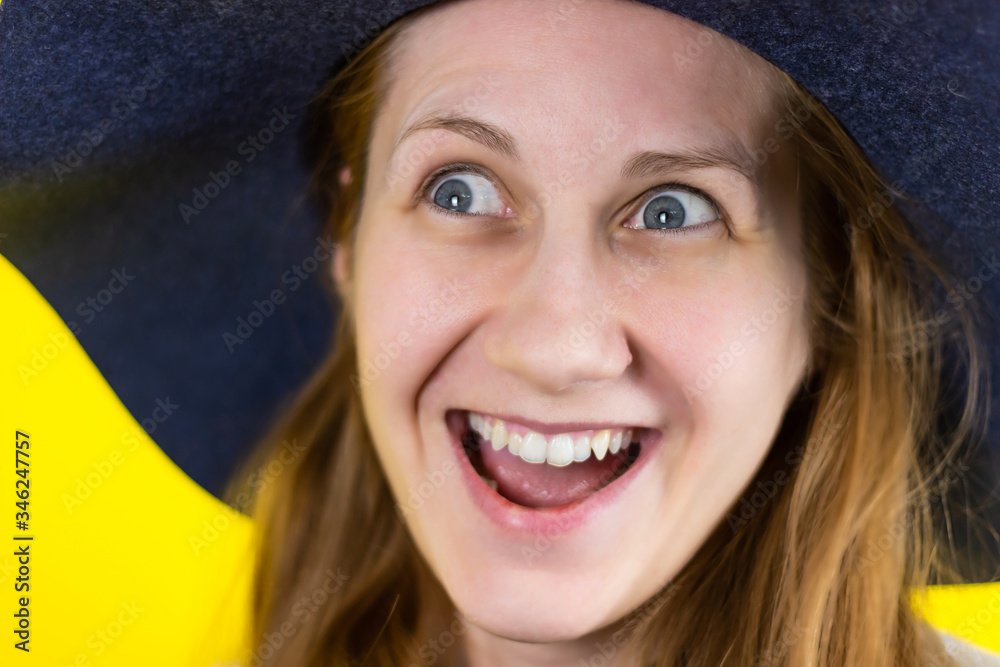 Close-up Portrait of a young beautiful red-haired girl smiling broadly and looking playfully to the side. on his head is a blue hat. On a yellow background . Close-up Portrait of a young beautiful red-haired girl smiling broadly and looking playfully to the side. on his head is a blue hat. On a yellow background .