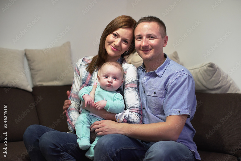 Young couple sitting on couch with his 3 months old baby boy, posing for family photo Young couple sitting on couch with his 3 months old baby boy, posing for family photo
