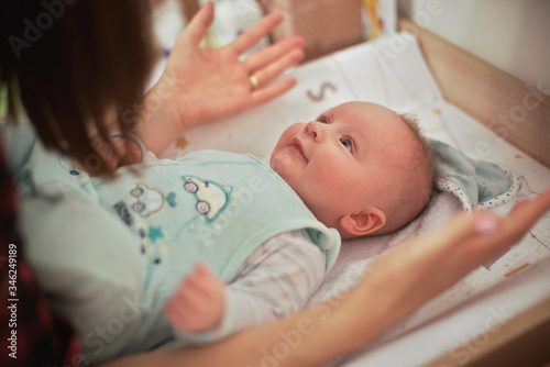 4 months old infant baby boy at changing table, mother playing with him, detail from above