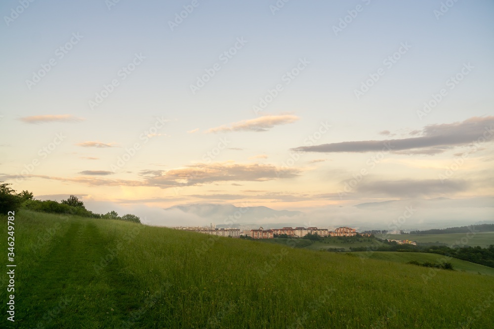 Sunrise and sunset, beautiful clouds over the meadow, hills and buildings in the town. Slovakia