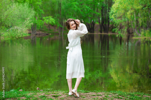 Portrait of a young beautiful woman in white dress posing by the lake © Andrey_Arkusha