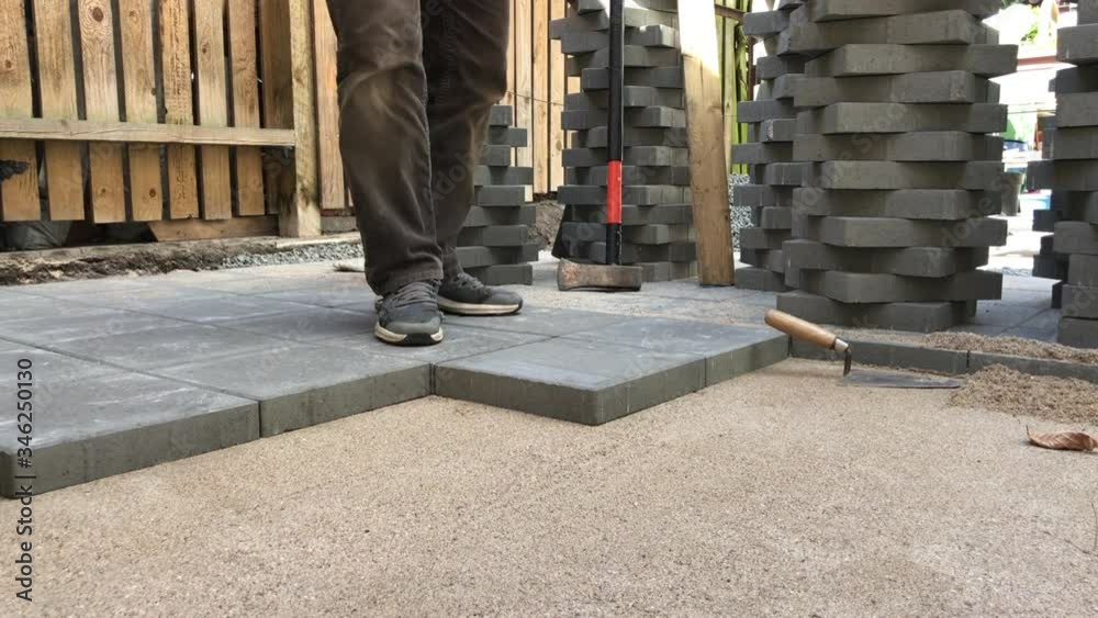 Man laying rows of concrete square pavers or tiles nicely laid in prepared flat sand surface. Work seen from below - worms perspective.