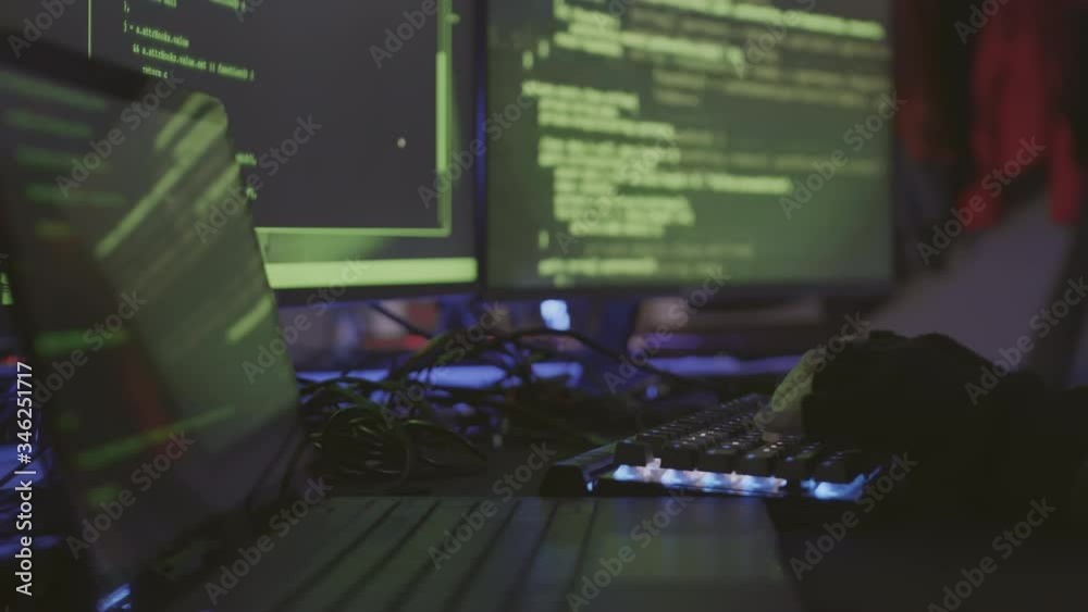 Close up of hands of unrecognizable coder sitting in dark room and developing program code on different computers