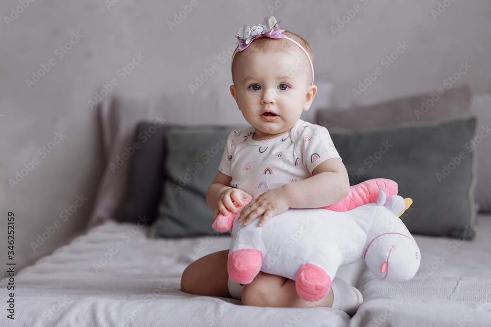 adorable little girl is playing with toy unicorn on bed at home. concept of childhood day. happy baby's, family day adorable little girl is playing with toy unicorn on bed at home. concept of childhood day. happy baby's, family day