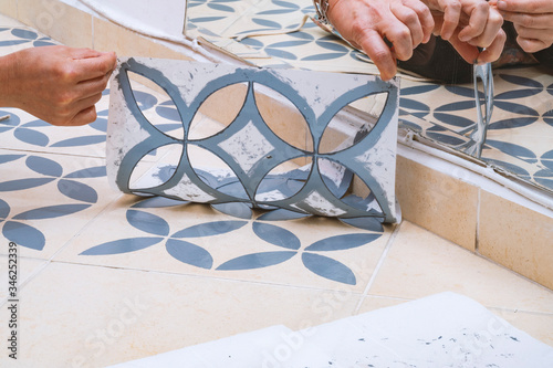 Stay at home and home improvement concept: Close up of hands removing a decorative painting stencil with a vintage design from the floor tiles after successfully painted into gray.