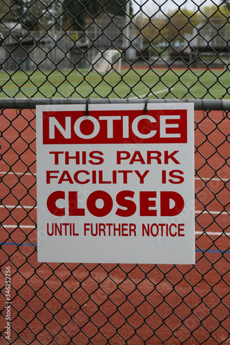 Vertical color photograph of a closed sign attached to the fence of a track and turf field