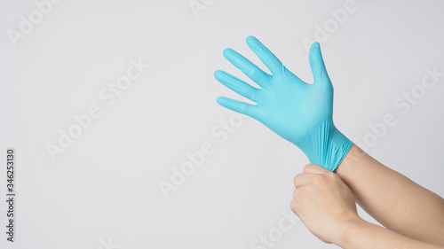 Left hand is pulling right hand wearing blue latex gloves on white background. © nisara