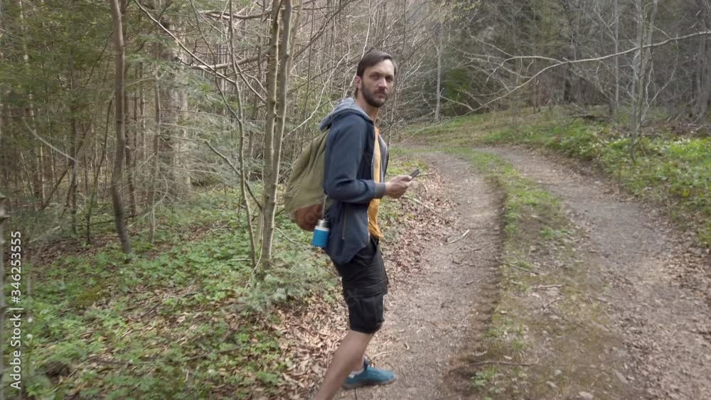 Male traveler walking at the forest using smartphone for navigation stops and exploring the area. Recreation at the nature Male traveler walking at the forest using smartphone for navigation stops and exploring the area. Recreation at the nature
