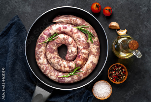 raw spiral sausage in a pan with spices and rosemary on a stone background