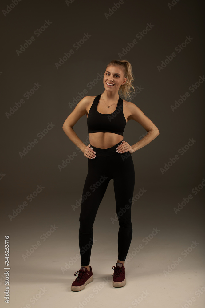 Happy young woman in sports clothing smiling. Muscular fitness model on grey background looking away at copy space. Trained body.