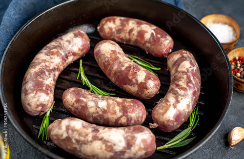 raw sausages in a pan with spices and rosemary on a stone background