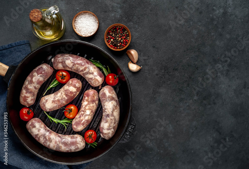 raw sausages in a pan with spices and rosemary on a stone background with copy space for your text