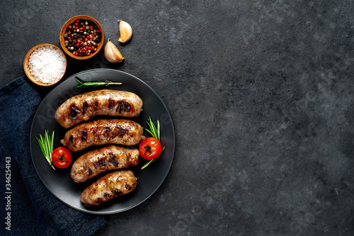 grilled sausages with spices and rosemary in a black plate on a stone background with copy space for your text