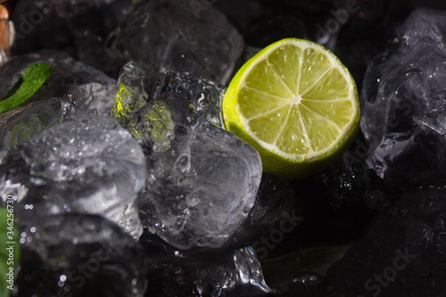 Lemon slice in ice cubes on a black background with mint closeup. Citrus sour fruit. Concept of freshness, cold fresh drinks, rest and relaxation. Half of lime. Cool down.