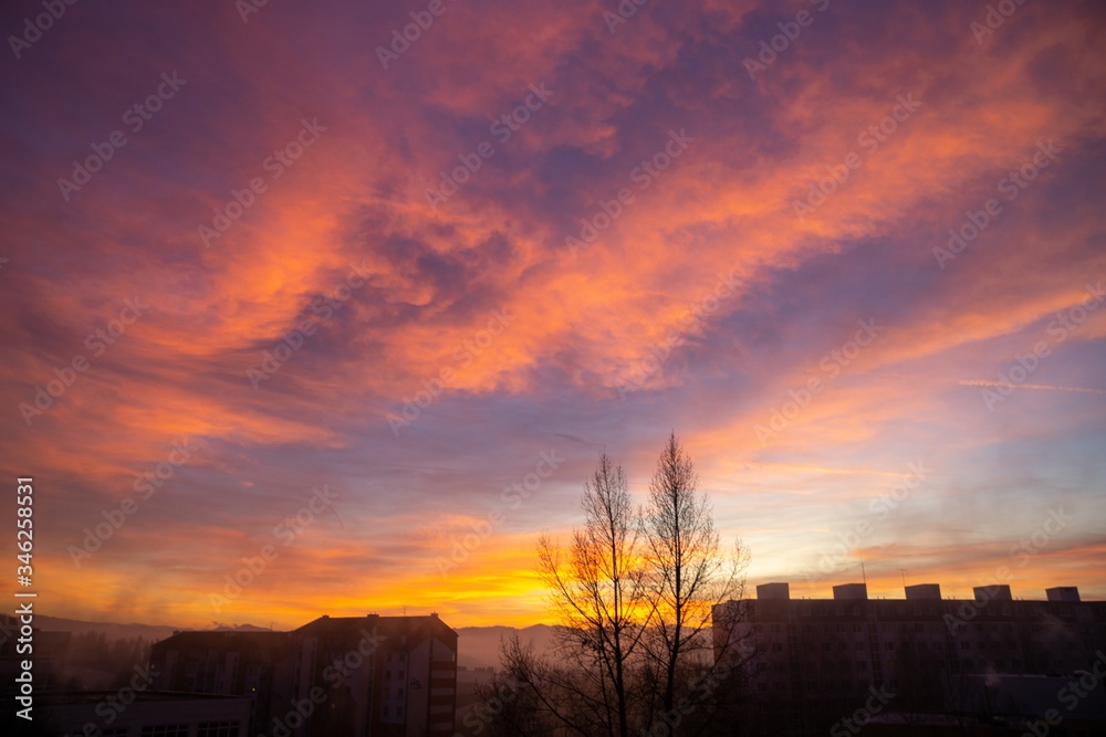 Fototapeta premium Sunrise and sunset, beautiful clouds over the meadow, hills and buildings in the town. Slovakia