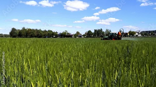 tractor cultivate field, tractor spraying vineyard with fungicide, sprayer machine, trailed by tractor, sprinkles pesticides among rows of grain