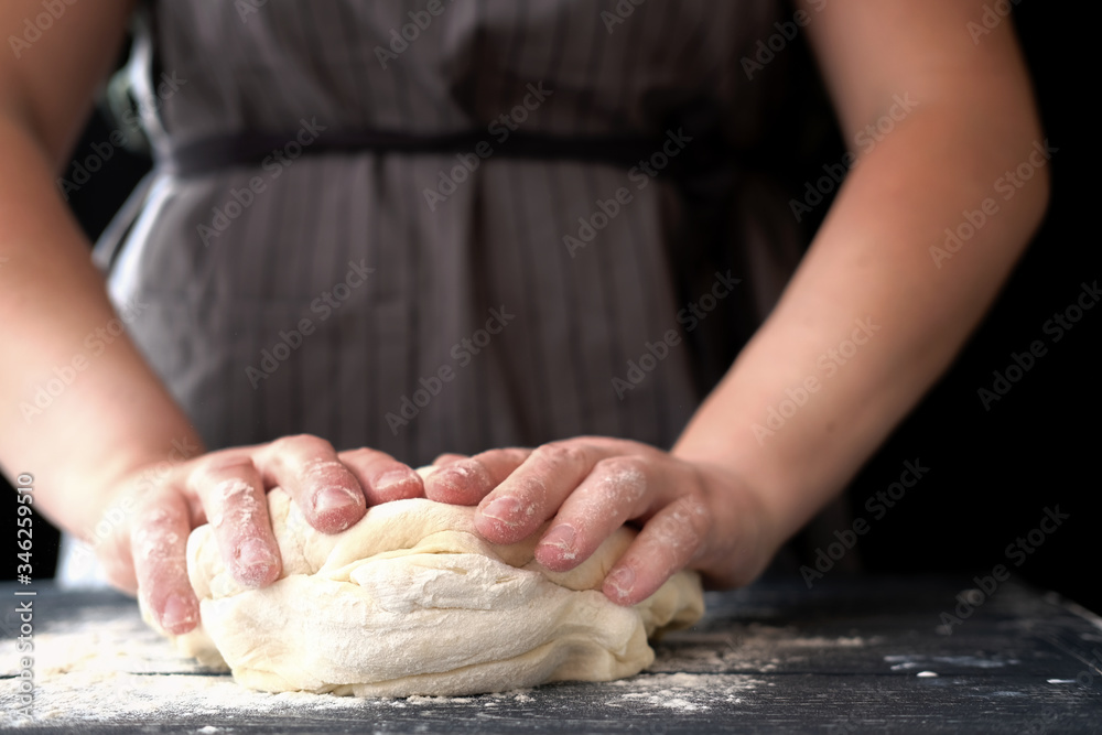 woman chef kneading dough for bread or pizza. bakery or homemade bread in process, woman in grey apron against black background. Concept of baking and patisserie. woman chef kneading dough for bread or pizza. bakery or homemade bread in process, woman in grey apron against black background. Concept of baking and patisserie.