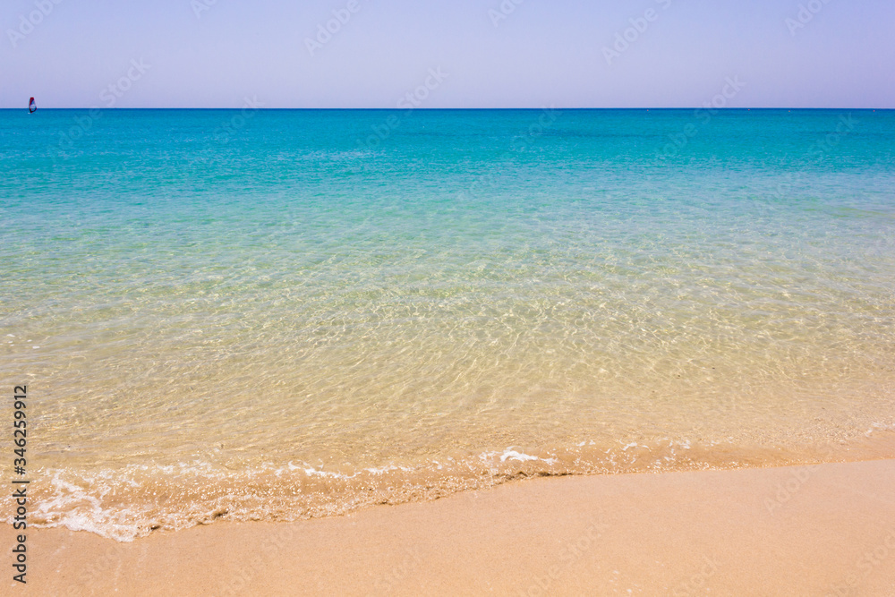 Fresh crystalline water seashore with windsurfer sailing far away in Fuerteventura. Idyllic natural landscape view of turquoise water empty beach. Lost in paradise, sport activity practice concepts