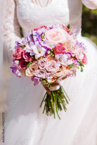 Bridal morning details. Bride with colorful wedding bouquet. Wedding beautiful bouquet in the hands of the bride, selection focus. Girl in white wedding dress holding bunch of flowers outdoors. 