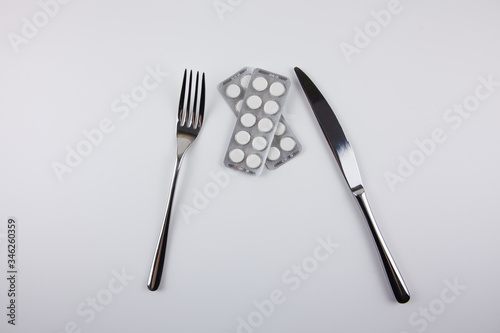 Iron fork and knife with pills on a white background. Use of medications. Care of health. Excessive use of medications during treatment. Eating pills.