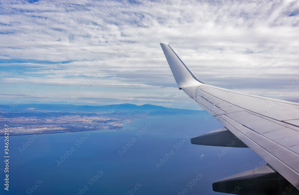 View of the wing of an airplane flying above the clouds at high altitude under a blue sky from the passenger window. In flight over Europe. View of jet airplane wing flying in blue sky over clouds. View of the wing of an airplane flying above the clouds at high altitude under a blue sky from the passenger window. In flight over Europe. View of jet airplane wing flying in blue sky over clouds.