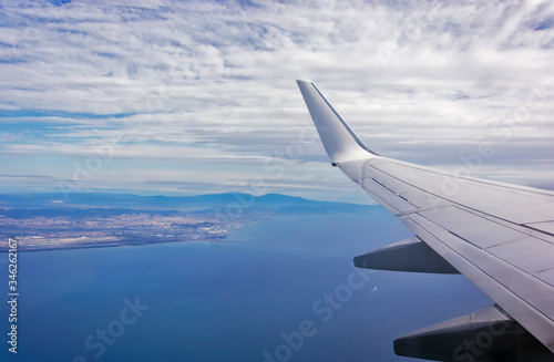 View of the wing of an airplane flying above the clouds at high altitude under a blue sky from the passenger window. In flight over Europe. View of jet airplane wing flying in blue sky over clouds. photo