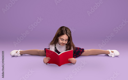 Schoolgirl doing splits and reading textbook photo