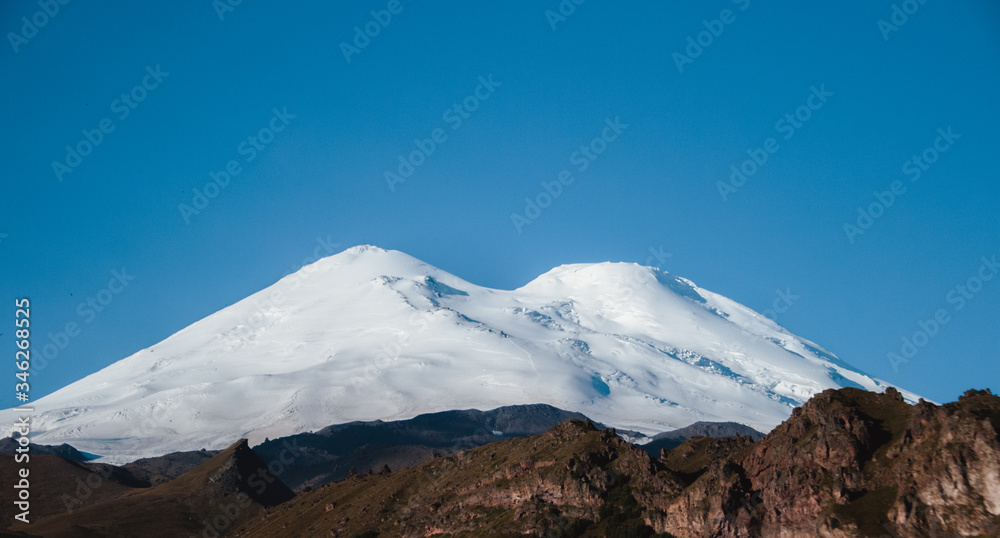 Snow-white Elbrus against a clear blue sky. National Park of Elbrus region. Dormant volcano. The highest mountain in Europe.