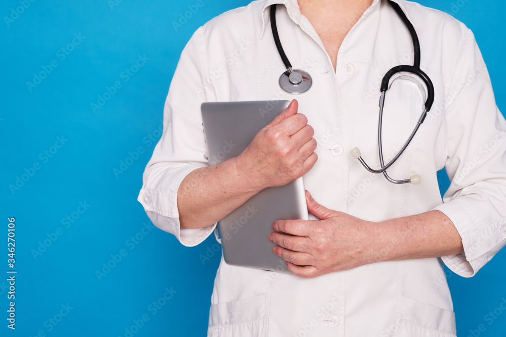 Eldery caucasian doctor lady in white coat and with stethoscope and tablet on blue background. Emotional portraits Eldery caucasian doctor lady in white coat and with stethoscope and tablet on blue background. Emotional portraits