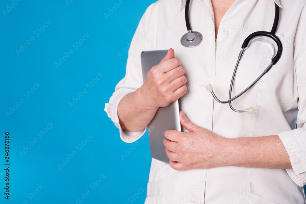 Eldery caucasian doctor lady in white coat and with stethoscope and tablet on blue background. Emotional portraits Eldery caucasian doctor lady in white coat and with stethoscope and tablet on blue background. Emotional portraits