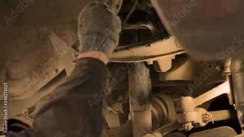 Hands in gloves and work clothes are repairing a spare part of a car in a garage, closeup.