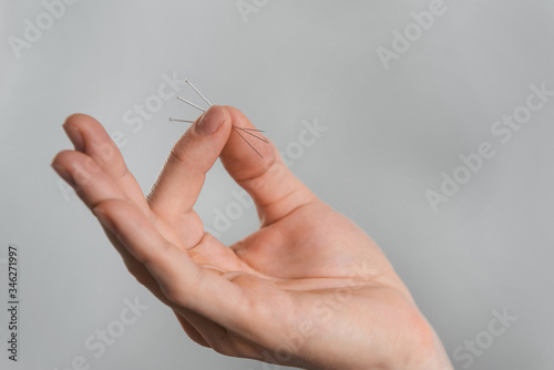 Acupuncture needles in hands over grey background.