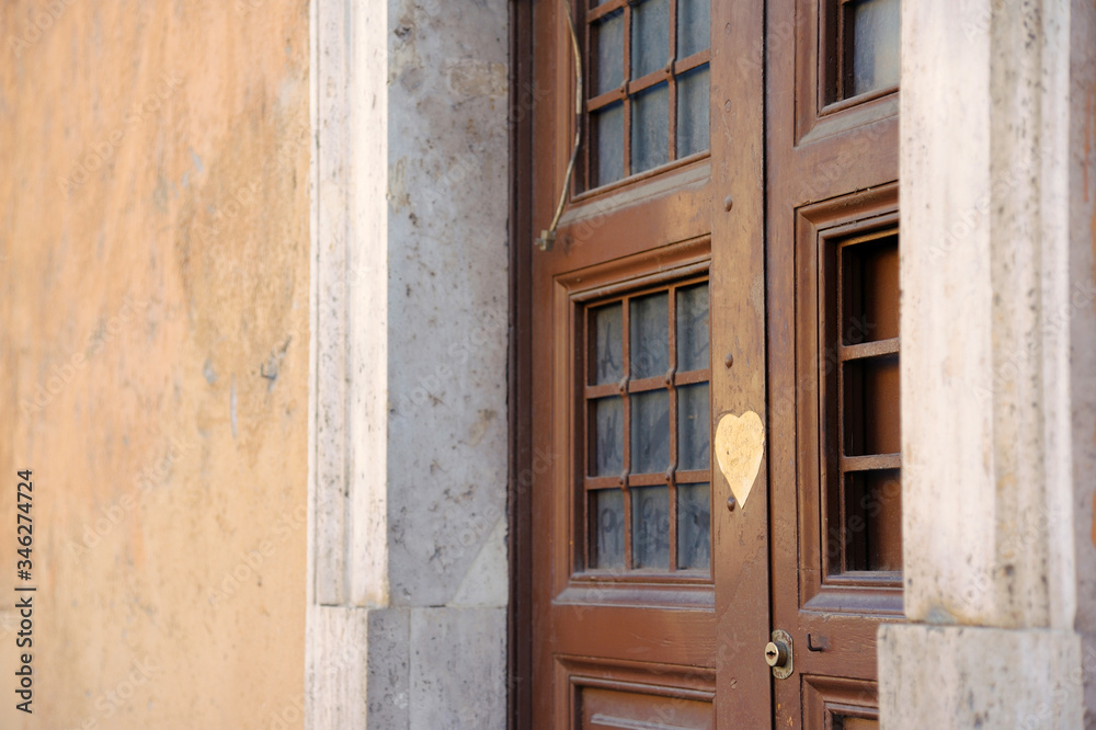 Rome, Italy - February 24, 2012: .Ancient brown wooden door of one of the old houses of Rome. There is a window with bars on the door. Heart sticker on the door Rome, Italy - February 24, 2012: .Ancient brown wooden door of one of the old houses of Rome. There is a window with bars on the door. Heart sticker on the door