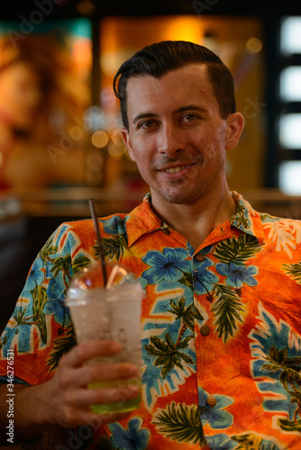 Happy young handsome tourist man holding drink inside restaurant