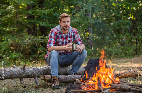 man relaxing in park. hiking adventure. picnic in tourism camp. drink coffee at picnic campfire. get warm near fire. ranger at outdoor activities. hiking and camping. spend picnic weekend in nature