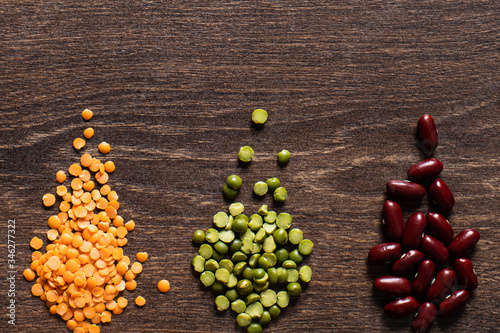 Three types of legumes  beautifully laid out on a wooden background - red beans  green peas and orange lentils. Top view. copy space.. Vegetarian food.