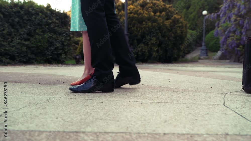 Legs of a guy and a girl in a dance. A guy in uniform and a girl in a blue dress are dancing a waltz in a park around an old suitcase. 4k